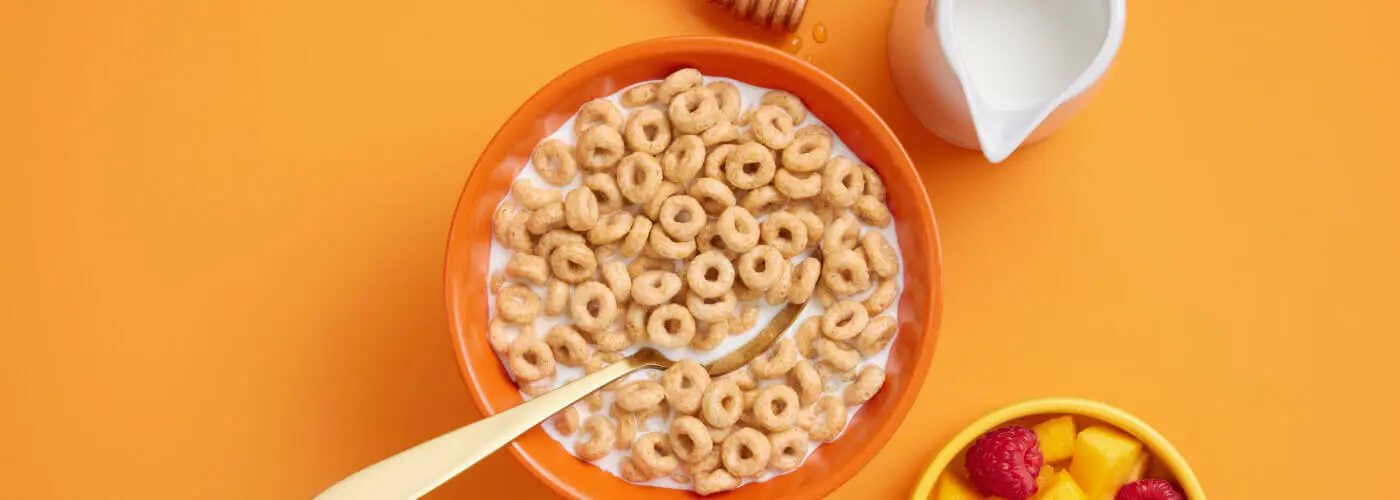 A bowl of cereal with milk and fruit on an orange background.