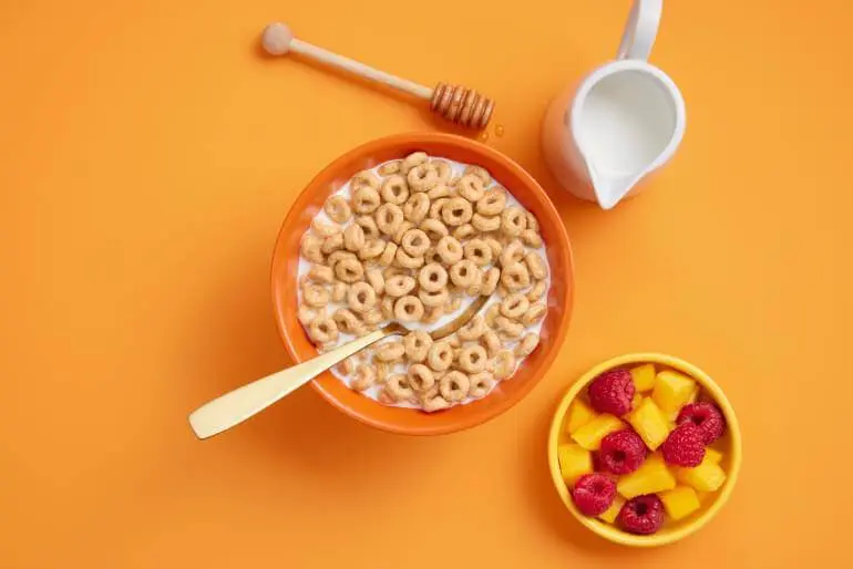 A bowl of cereal with milk and fruit on an orange background.
