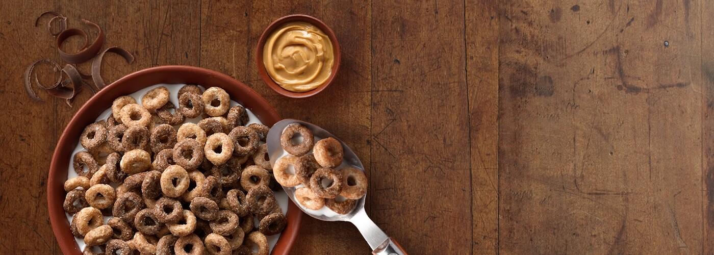 Un bol de céréales Cheerios au beurre de cacahuète et au chocolat avec une tasse de beurre de cacahuète et une cuillère.