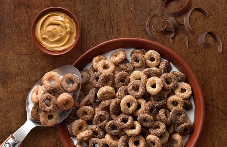 Un bol de céréales Cheerios au beurre de cacahuète et au chocolat avec une tasse de beurre de cacahuète et une cuillère.