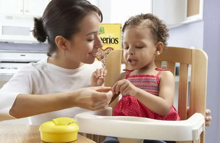 A woman and child sitting in a high chair, eating a bowl of Cheerios