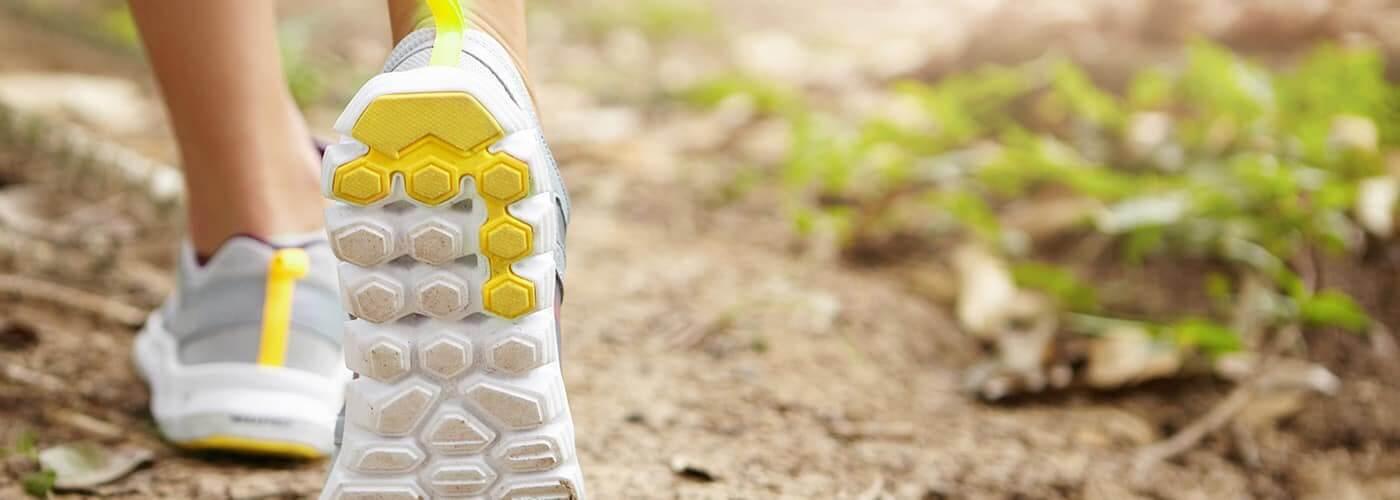 A close-up of a person's athletic shoes walking on a trail.