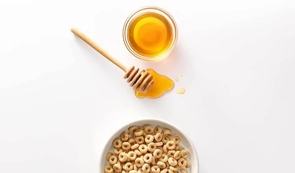 Fresh honey next to a bowl of Cheerios.